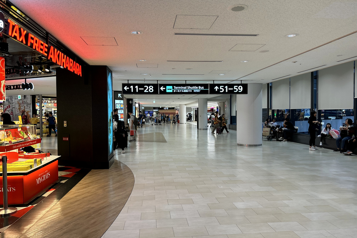 Travelers walking through a Narita Airport Terminal 1 corridor beneath terminal shuttle signs