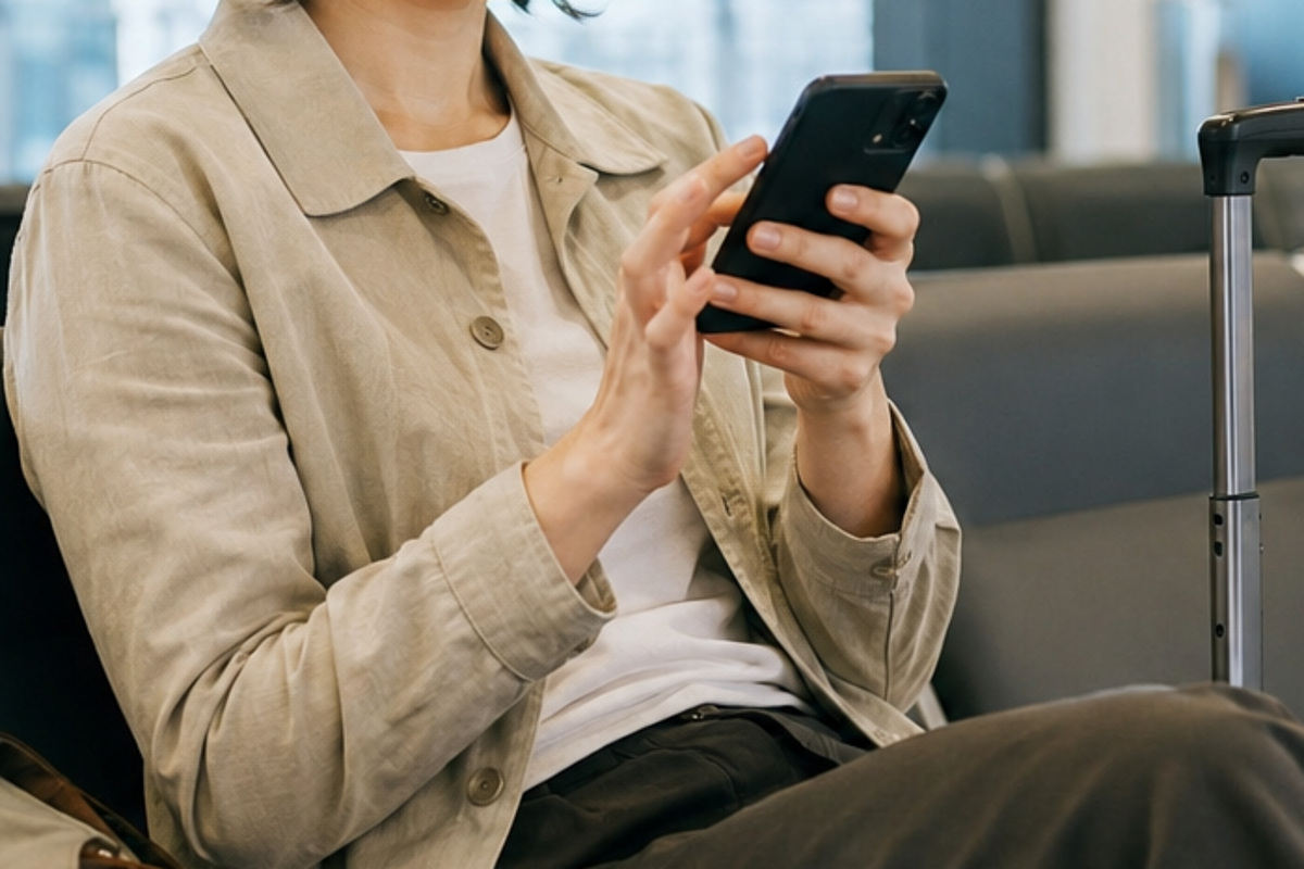 Traveler setting up mobile data on a phone at the airport with luggage beside them