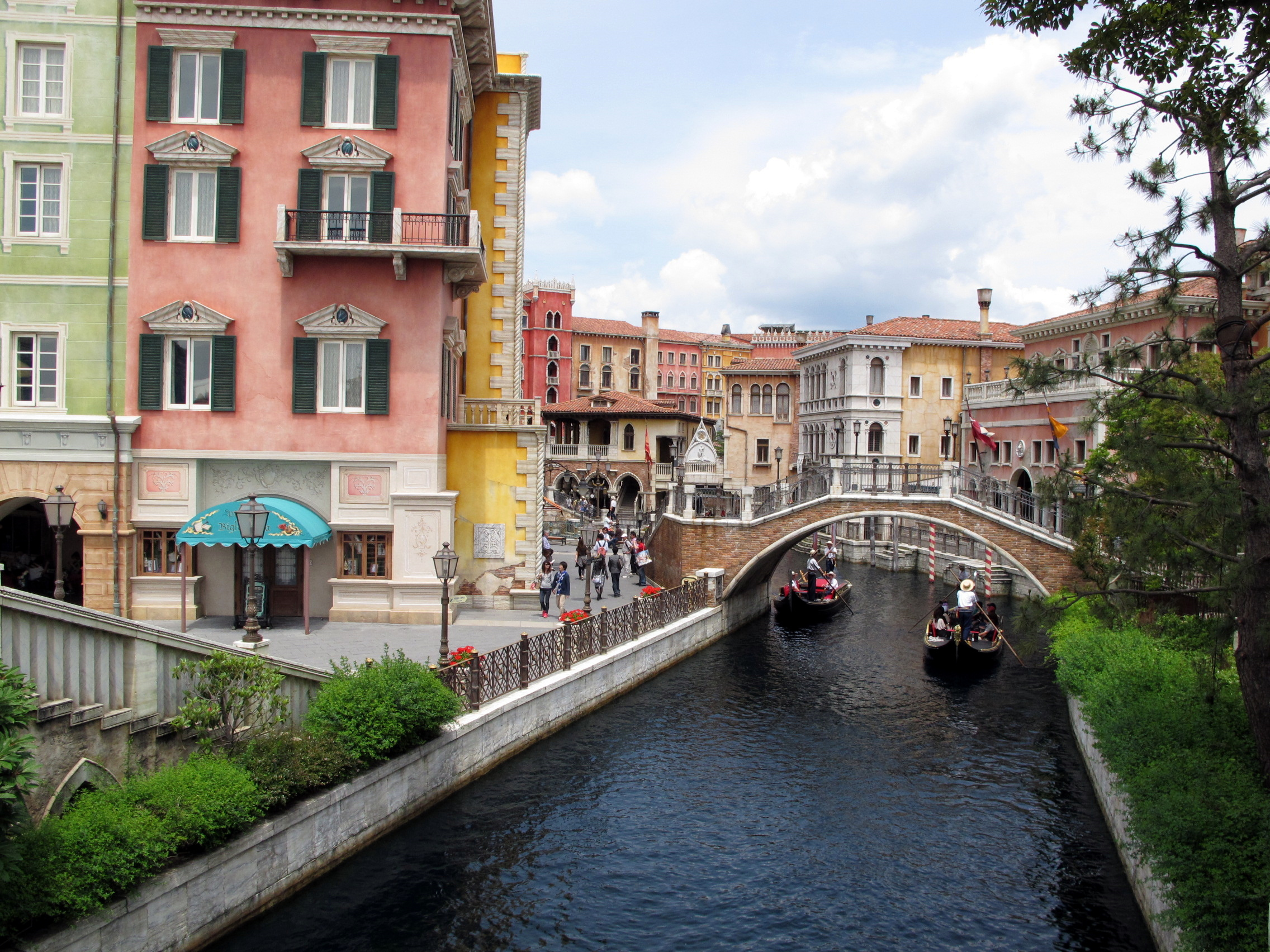 Gondoliers guide boats beneath a stone bridge between colorful buildings along Palazzo Canals.