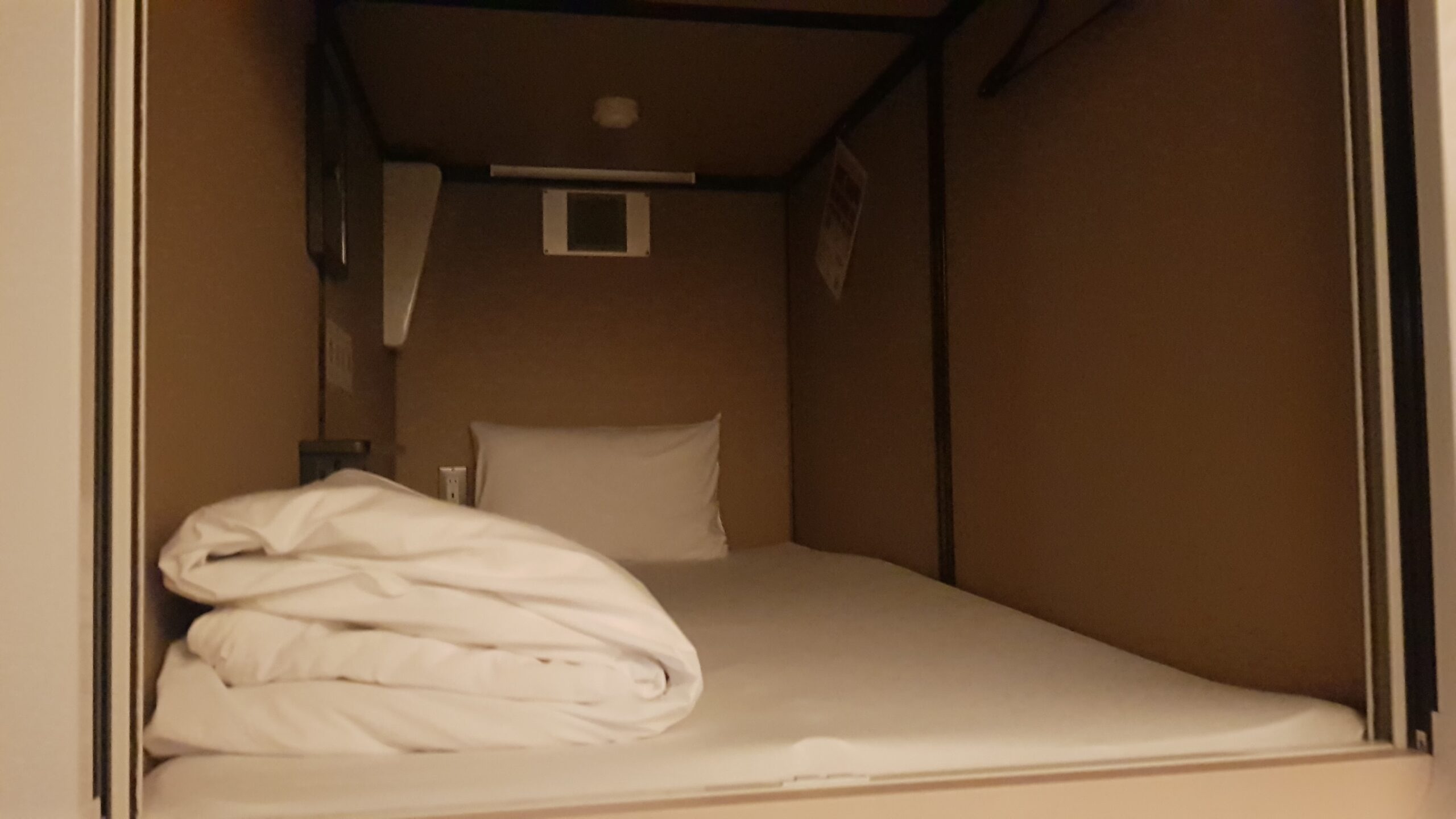 Bedding and controls inside a capsule hotel sleeping pod
