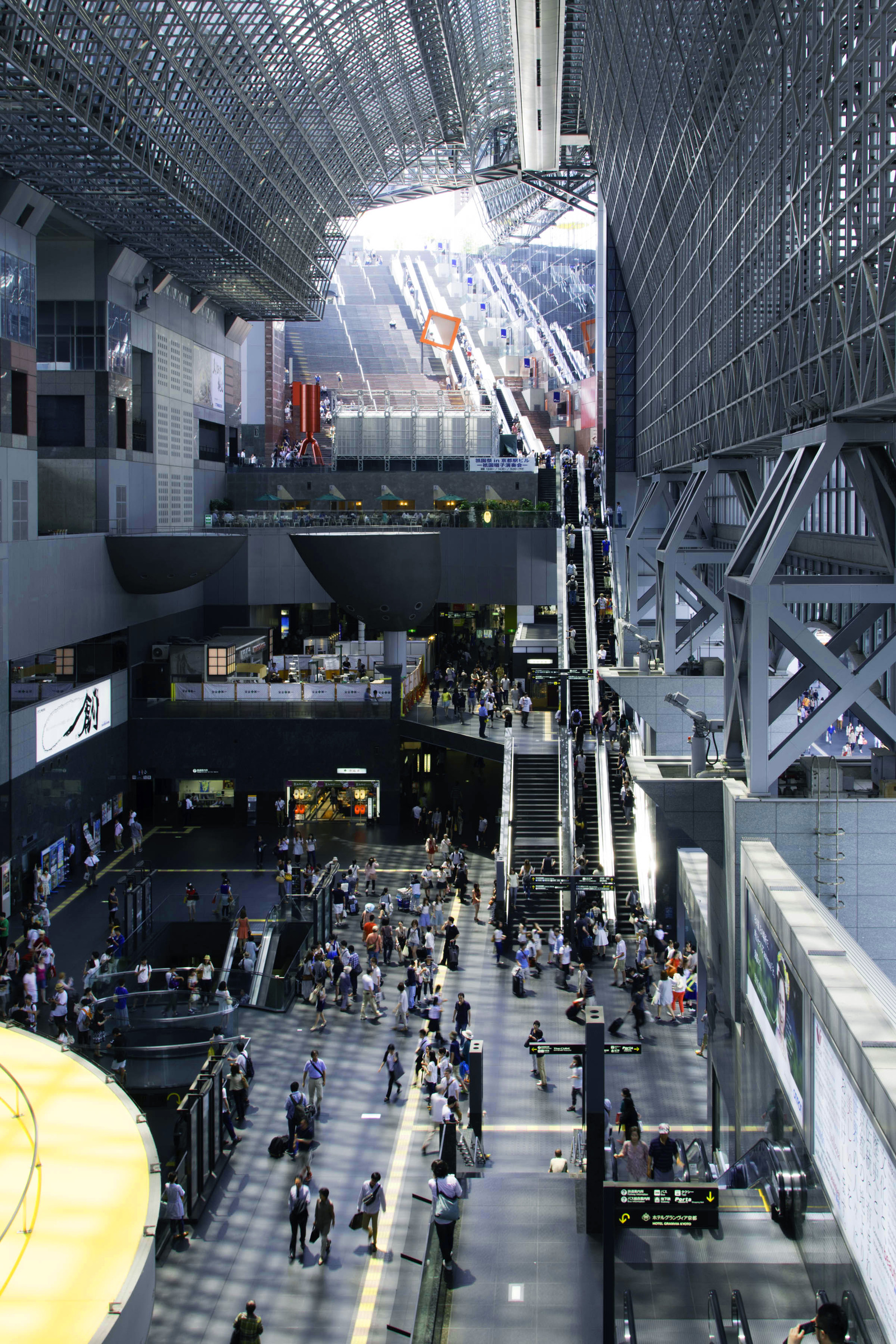 Travelers and escalators beneath the tall steel-and-glass atrium of Kyoto Station.