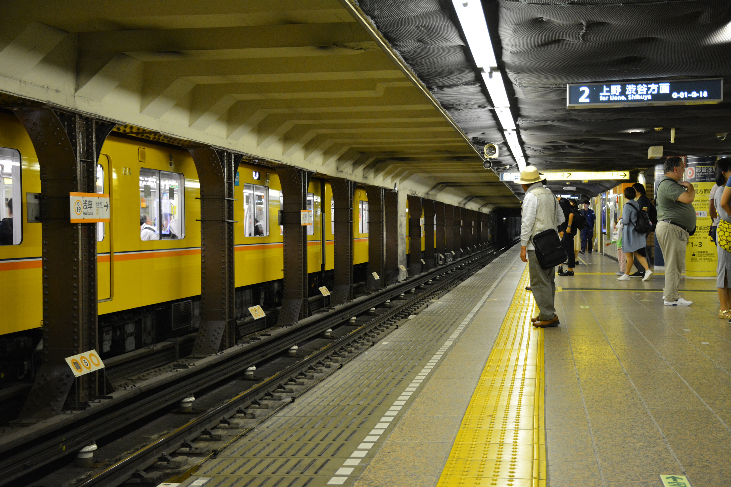 Passengers wait on an Asakusa Station platform beside a yellow Ginza Line train.