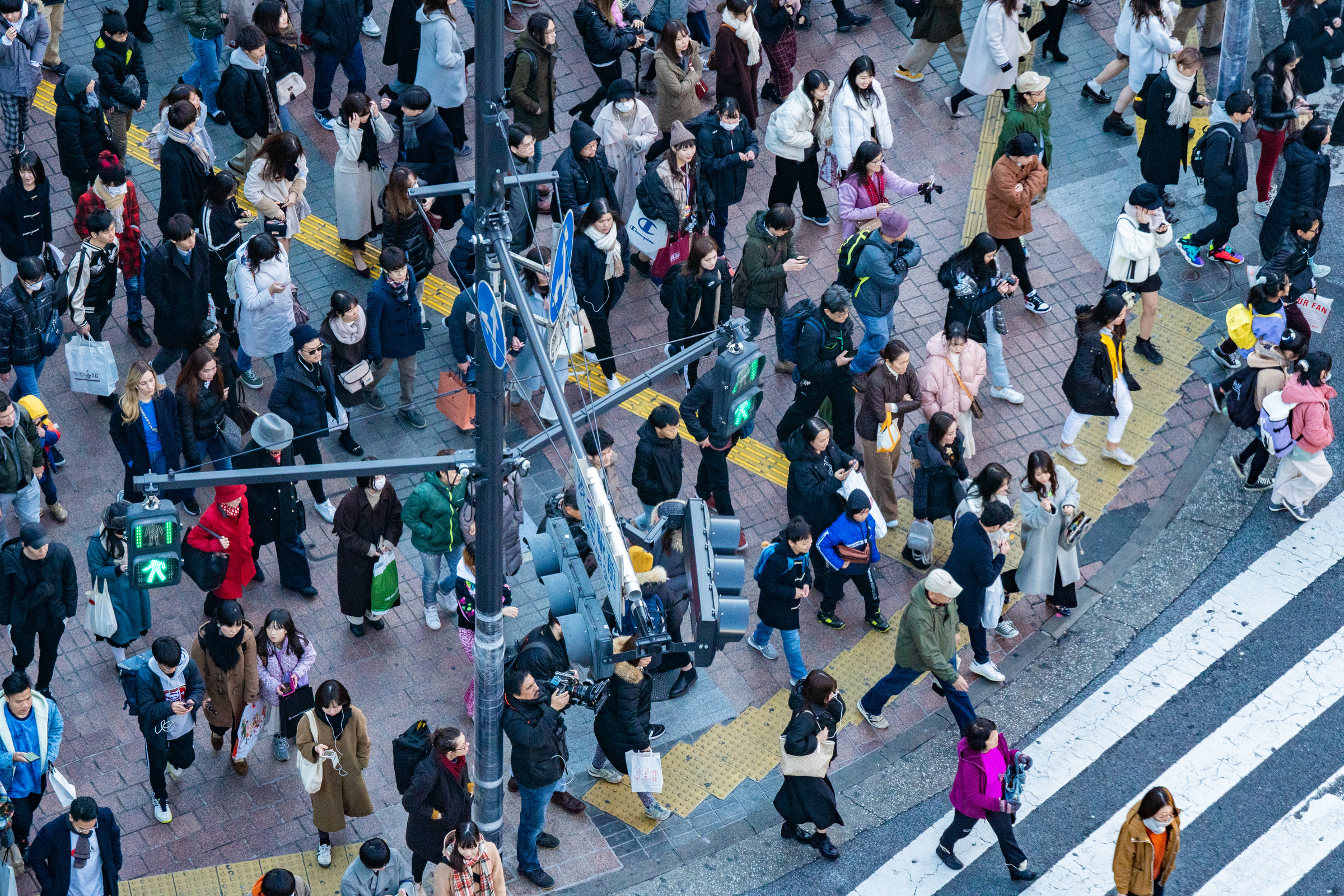 People begin crossing at Shibuya as green pedestrian signals light up, viewed from above.
