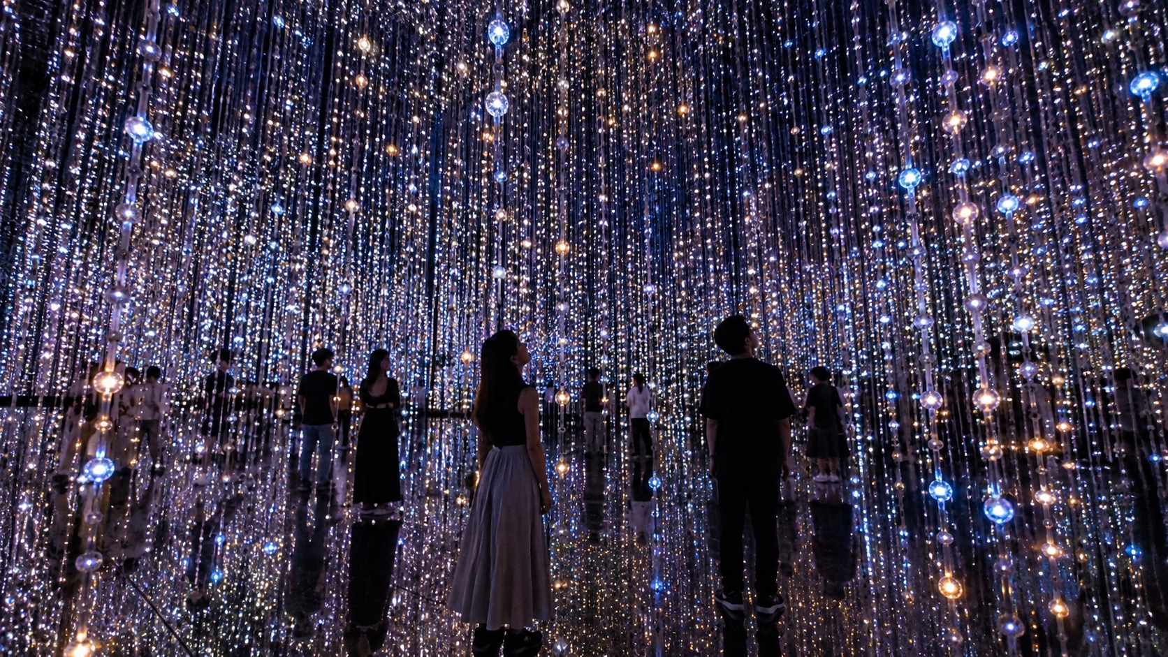 Visitors standing inside a mirrored room filled with hanging lights
